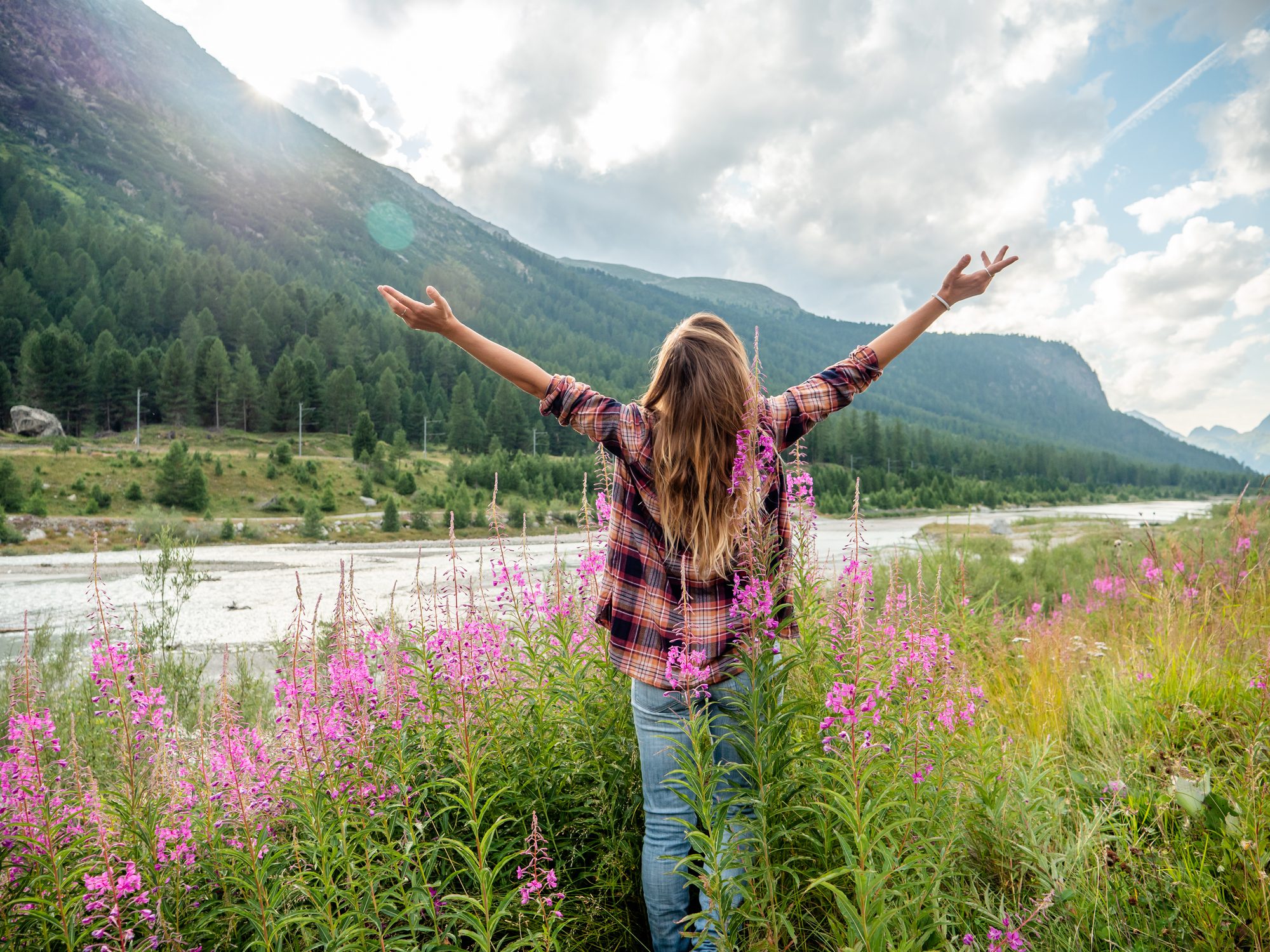 A woman with outstretched arms enjoys a scenic mountain and river view.